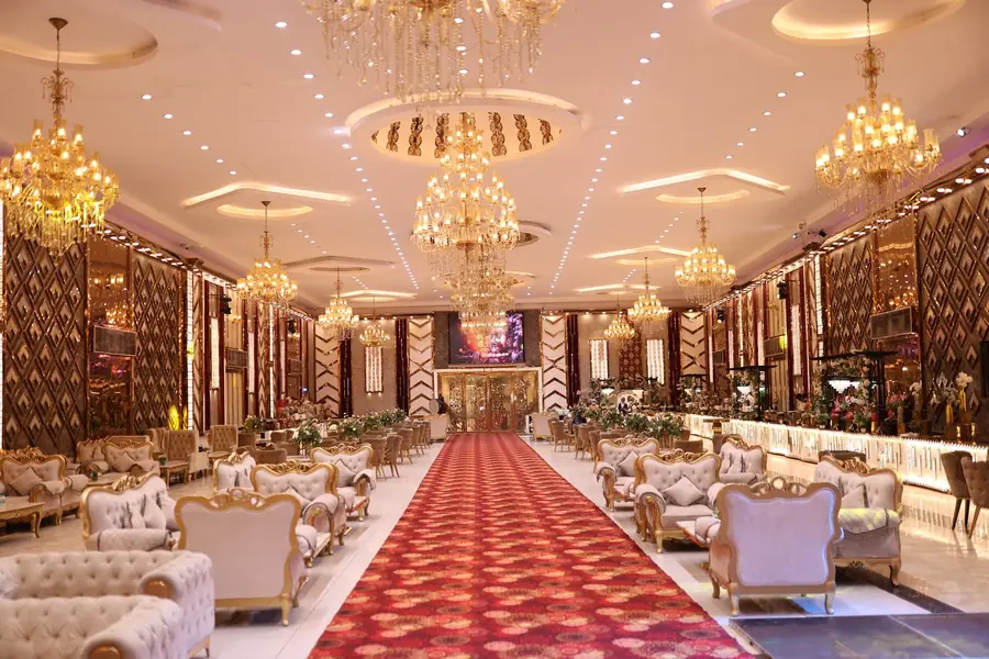 Grote feestzaal met gouden kroonluchters, spiegelwanden en een breed looppad in het midden
